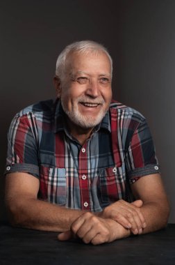 Karizmatik gömlekli yaşlı bir adam gri bir arka planda neşeyle gülüyor, yakın plan portresi yapıyor.