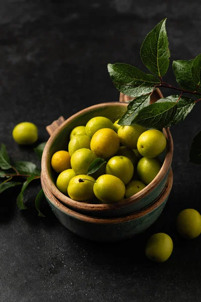 Sarı, taze koparılmış kiraz eriği, yeşil yapraklar seramik bardaklarda gri arka planda, metin için yer var.