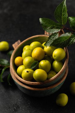 Sarı, yeni koparılmış kiraz eriği, yeşil yapraklı, seramik bardaklarda gri arka planda, yakın planda.