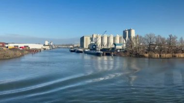 Maas Nehri, kıyıdan gelen bir tekneden görüldü ve arka planda mavi gökyüzünde bir fabrikanın kuleleri vardı.