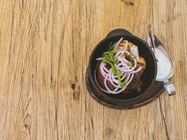 Pirzola, sebze ve beyaz et sosu kırsal bir ahşap tahtada servis edilen dökme demir bir tavada. Sağlıklı gurme yemek konsepti. Dizinin bir parçası. Boşluğu kopyala.