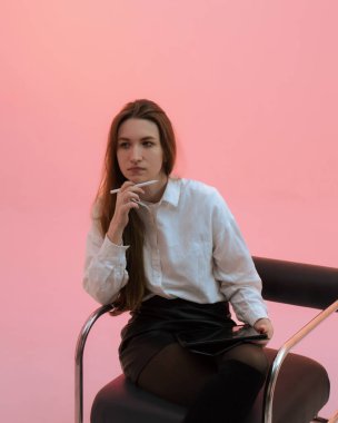 Beyaz gömlekli, beyaz tişörtlü çekici genç bir kadın, bir stilus ile yüze dokunuyor ve soluk pembe arka planda izole edilmiş dijital bir tablet tutuyor. Dijital çizim. Beyin fırtınası. Bir serinin parçası.