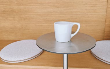 Beyaz fincan taze siyah filtre kahve ya da yumuşak yastıklı bir demet yastığın önünde metal yuvarlak bir masanın üzerinde kapuçino. Yan görüş, kopyalama alanı. Kahve dükkanı, sıcak içecek konsepti. Bir serinin parçası.