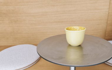 Sarı kahve ya da kapuçino. Yumuşak yastıklı bir demet yastığın önünde metal yuvarlak bir masanın üzerinde yarı sarhoş halde duruyor. Yan görüş, kopyalama alanı. Kahve dükkanı, sıcak içecek konsepti. Bir serinin parçası.