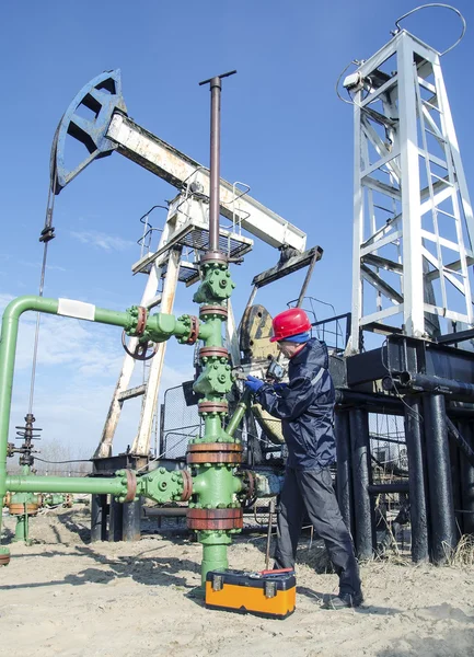 Trabajador de yacimientos petrolíferos cerca de pozo cabeza y bomba jack — Foto de Stock