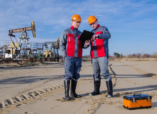 Oilfield workers near pump jack and well head — Stock Photo, Image