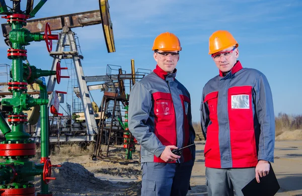 Trabajadores de yacimientos petrolíferos cerca de gato de bomba y cabeza de pozo —  Fotos de Stock