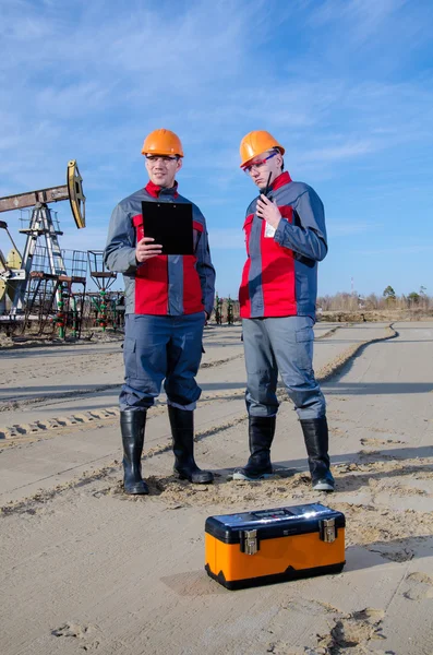 Trabajadores de yacimientos petrolíferos cerca de gato de bomba y cabeza de pozo — Foto de Stock