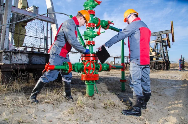 Oilfield workers near pump jack and well head — Stock Photo, Image