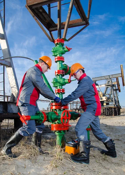 Oilfield workers near pump jack and well head — Stock Photo, Image