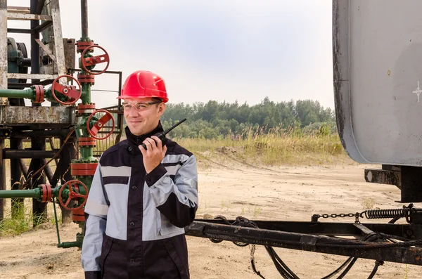 Operaio vicino a pompa, testa di pozzo e rimorchio serbatoio nel giacimento petrolifero . — Foto Stock