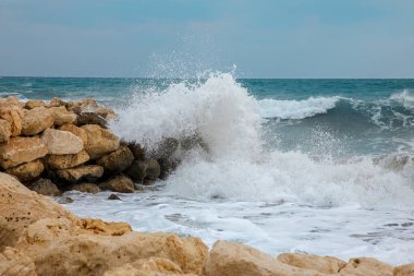 Dalgalar deniz kenarındaki kayalara çarpıyor.