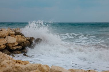 Dalgalar deniz kenarındaki kayalara çarpıyor.