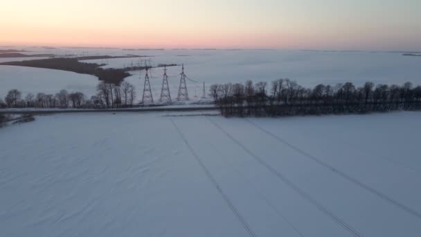 Vista aérea do drone em linhas de energia sobre o campo nevado no por do sol — Vídeo de Stock