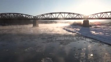 Sinematik İHA Çekimi, Donmuş Nehir üzerinde İleri Uçar ve Güneş Doğarken Kızıl Çelik Köprü Altında Hava 4k Görüntüsü