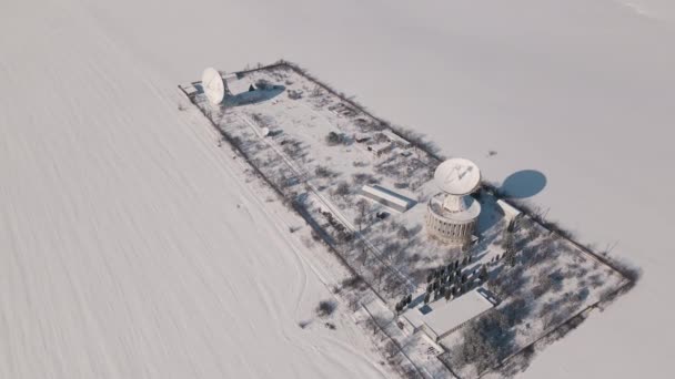 Widok z lotu ptaka na stację komunikacji kosmicznej w pokrytym śniegiem polu w słoneczny zimowy dzień, lot dronem nad obiektem strategicznym — Wideo stockowe