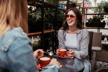 Açık havada kahve içen iki genç kadın, öğle yemeği konsepti, odak noktasında esmer kız.