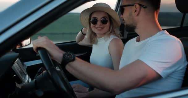 Feliz pareja joven sentada dentro de su coche y disfrutando de un viaje por carretera, viaje y aventura Concepto — Vídeos de Stock