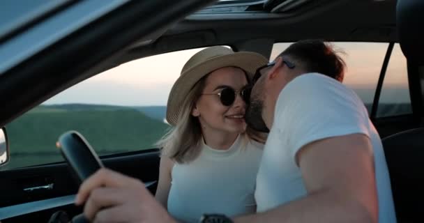 Ευτυχισμένο νεαρό ζευγάρι κάθεται μέσα στο αυτοκίνητό τους και φιλιά, απολαμβάνοντας οδικό ταξίδι, ταξίδια και περιπέτεια Concept — Αρχείο Βίντεο