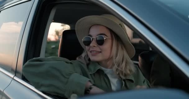 Прекрасна подорожня дівчина у капелюсі та сонцезахисних окулярах сидячи в автомобілі, насолоджуючись дорожньою подорожжю біля Каньйону — стокове відео