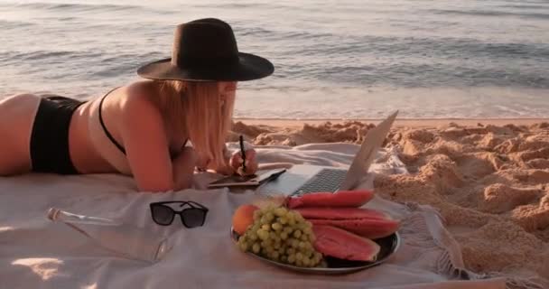 Close Up Side View of Young Woman Dressed Swimsuit and Hat Lying on the Sandy Sea Beach, Having Picnic at Sunrise Dawn and Working on Graphics Tablet and Laptop, Freelance and Remote Working Concept — Stok Video