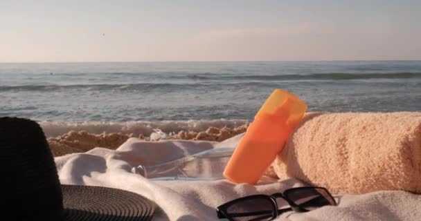 Zonnebrandcrème, Handdoek, Waterfles, Zonnebril en Hoed Liggend op deken op het Zandstrand bij zonsopgang, Zomervakantie en Zonnebaden Concept — Stockvideo