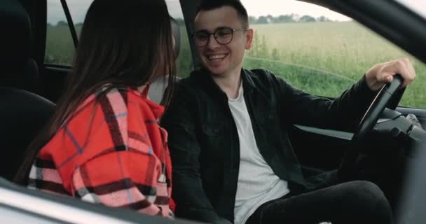 Casal jovem, cara com namorada sentada no carro, sorrindo e rindo, aproveitando viagem de carro pelo campo — Vídeo de Stock