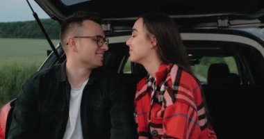 Genç çift, kız arkadaşıyla birlikte açık araba bagajında oturan, Kucaklaşan ve gülümseyen kırsal kesimde yolculuğun tadını çıkaran adam.