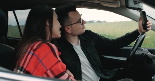 Fiatal pár, Guy with Girlfriend Ül az autóban, mosolygós és fotózás Selfie egy okostelefon, Élvezi Road Trip keresztül Vidéken — Stock videók