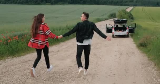 Back View of Young Couple Having Fun on a Road Trip, Girl with Her Boyfriend Holding by Hands and Running near Their Car in Countryside — 비디오