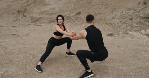 Deux athlètes en tenue de sport noire s'entraînent ensemble et font du squat en plein air, en mode de vie sain et en plein air Concept d'entraînement — Video