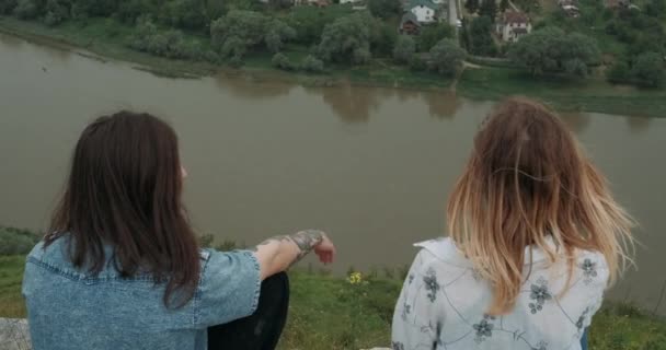 Fermer Retour Vue du jeune couple élégant, homme et femme tatoués aux cheveux longs tenant par la main alors qu'ils sont assis sur le bord du rocher près de la rivière, loisirs en plein air sains lors du jour d'été pluvieux — Video