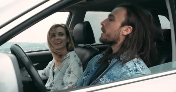 Dos jóvenes, hombre y mujer vestidos al estilo boho, sentados en su coche moderno, viaje por carretera y concepto de viaje — Vídeo de stock