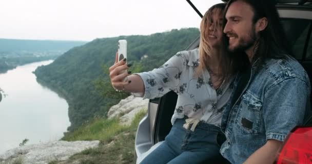 Dva pohlední cestovatelé, kteří si berou Selfie, zatímco sedí uvnitř auta kufru, stylový muž a mladá žena oblečená v Boho stylu těší Road Trip, Cestovní koncepce — Stock video