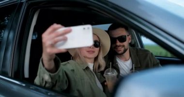 Kadın ve erkek arabalarında oturuyor, soğuk kahve içiyor ve akıllı bir telefonla selfie çekiyor, macera yolculuğunun tadını çıkarıyorlar.