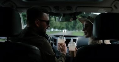 Genç adam ve kadının arabalarında oturup, soğuk kahve içip macera yolculuğunun tadını çıkarırken görüntüsü.
