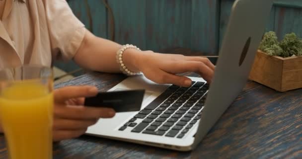 Vista lateral de la joven feliz con gafas usando el ordenador portátil y la tarjeta de crédito para hacer el pago en línea mientras está sentado en el café — Vídeos de Stock