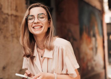 Gözlüklü Mutlu Genç Kadın gülümseyen ve şehirde yürürken akıllı telefon kullanan, Gözlüklü Sarışın Kız.