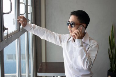 Asyalı işportacı büyük pencerelerden dışarı bakarken cep telefonuyla güvenle konuşuyor.