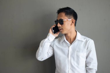 Asyalı Busin 'li adam gri arka planda telefonla konuşuyor.