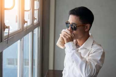 Düşünceli iş adamı buzlu kahve içiyor, pencereden bakıyor, manzaranın tadını çıkarıyor, toplantının başlamasını bekliyor, iş kararı veriyor, kopyalama alanı yaratıyor.