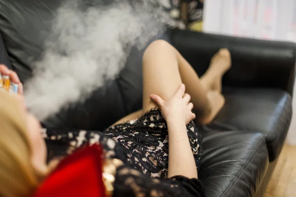 Chica en un sofá de cuero negro está fumando un cigarrillo electrónico — Foto de Stock