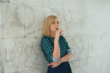 Genç sarışın kız arka plan duvar üzerinde elektronik sigara içiyor