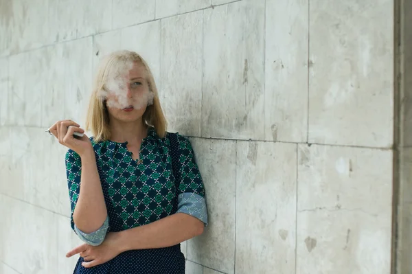 Giovane ragazza bionda fuma sigaretta elettronica sulla parete di sfondo — Foto Stock