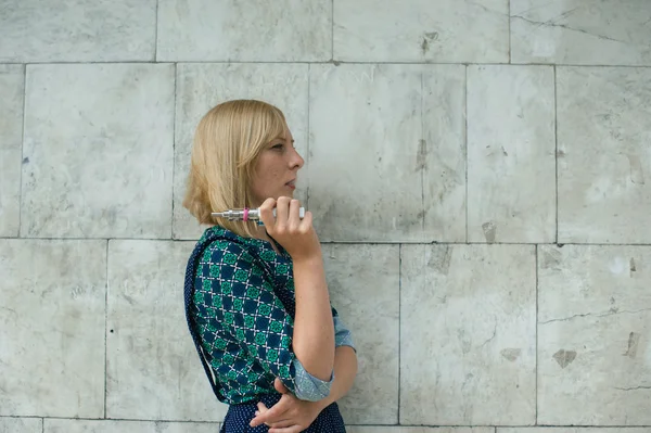 젊은 금발 소녀 배경 벽에 전자 담배를 피우는 — 스톡 사진