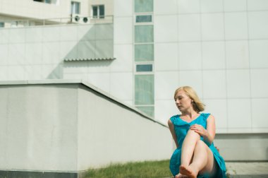 Genç sarışın kadın bacaklarını germe avluda bir bankta oturuyordu