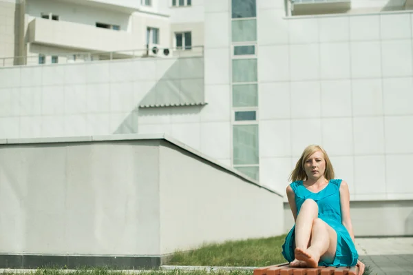 Jonge blonde vrouw zittend op een bankje in de binnenplaats die zich uitstrekt van haar benen — Stockfoto