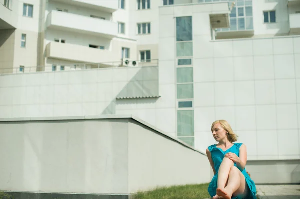 Jovem loira sentada em um banco no pátio esticando as pernas — Fotografia de Stock