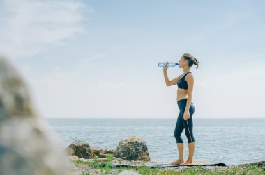 atletik kız içecekler su bir şişe bir çalışmadan sonra sahilde