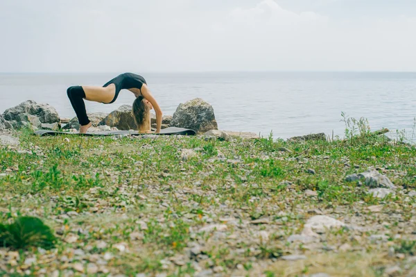Giovane donna è impegnata nella meditazione, stretching, yoga sullo sfondo della spiaggia — Foto Stock